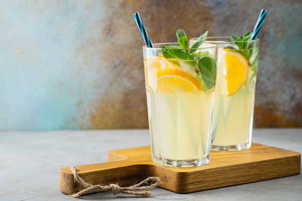 Two glass with lemonade or mojito cocktail with lemon and mint, cold refreshing drink or beverage with ice on rustic blue background. Copy space.